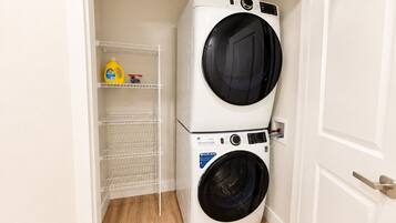 A laundry room with two stacked washing machines, a shelf with cleaning supplies, and a door.