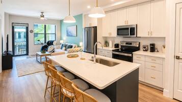 A modern kitchen with a central island, bar stools, and a dining area with a sofa and chairs.