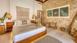 A spacious bedroom with a large bed, a stone wall, and framed tropical leaf artwork. - Villa Provence, NEW 8BDR, Jacuzzi, Cinema, Luxury (Kabupaten Badung)