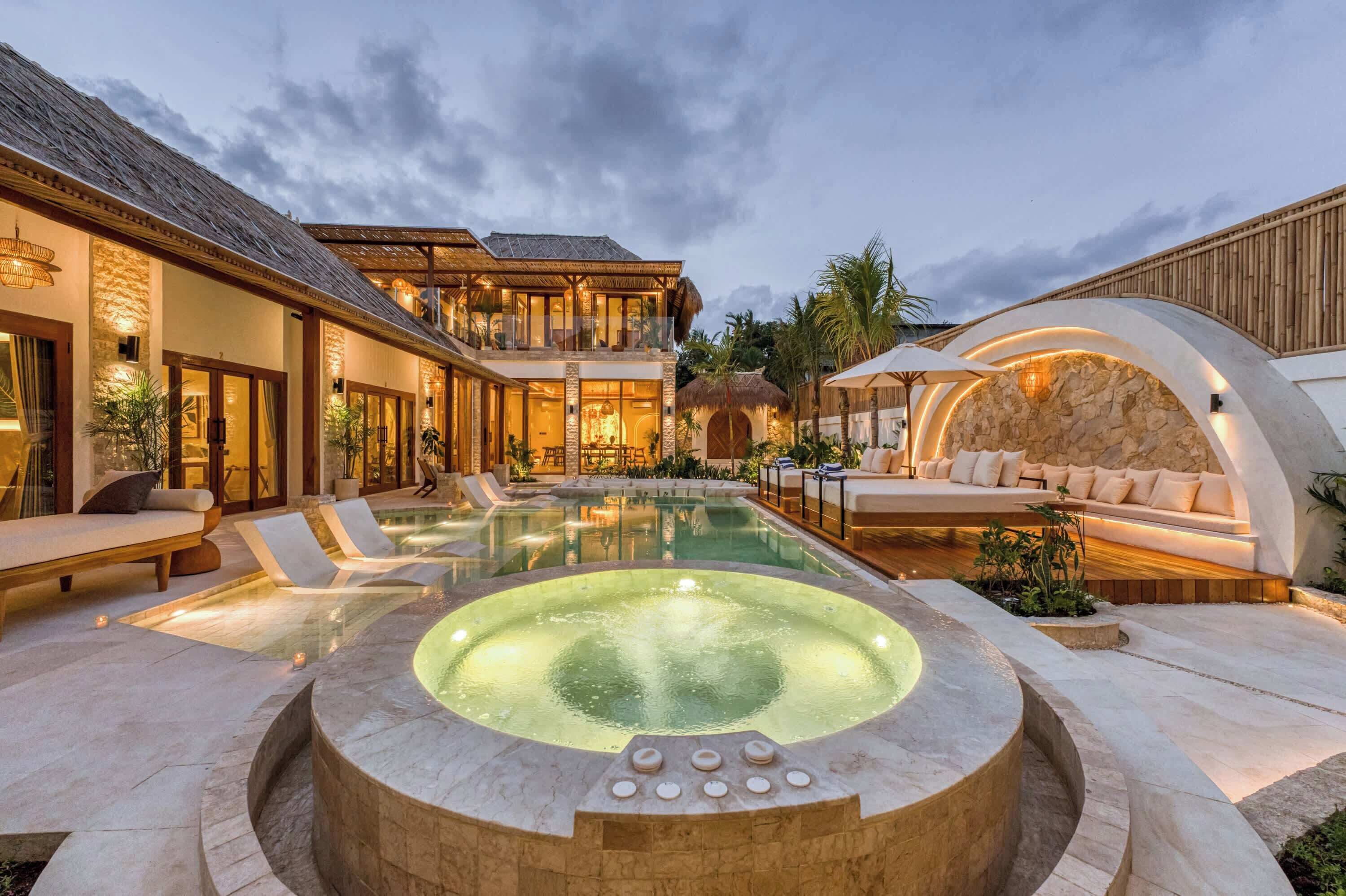Un espace extérieur luxueux avec une piscine, un jacuzzi, des chaises longues et un coin salon aménagé avec un mur en pierre.