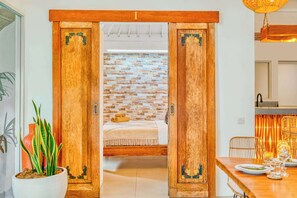 Ein Zimmer mit einem Bett, einer Holztür mit einer Nummer, einer Backsteinwand und einem Essbereich mit Stühlen und einem Tisch.