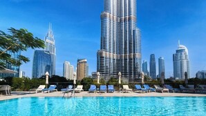 A swimming pool with lounge chairs and a city skyline in the background. - The Address Dubai Opera T1 - Skyline Luxe 1BR | Burj Khalifa & Dubai Mall (Downtown)