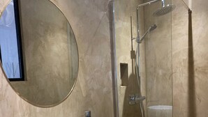 Uma casa de banho moderna com um espelho redondo, uma pia branca e uma cabine de duche em vidro.