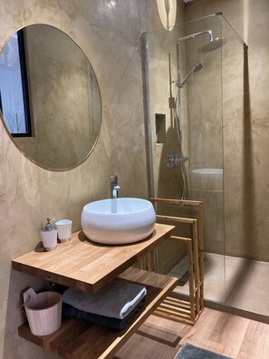 Une salle de bain moderne avec un miroir rond, un lavabo blanc et une cabine de douche en verre.