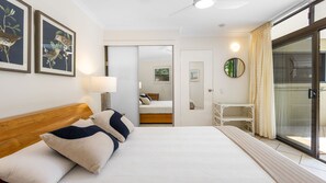A bedroom with a bed, bedside table, lamp, and a view through a sliding door to another room. - Bahia Lindo 1 Noosa Heads (Noosa Heads)