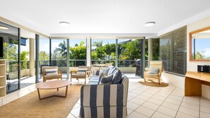 A spacious balcony with a sofa, chairs, and a dining table, offering a view of lush greenery and a clear sky. - Bahia Lindo 1 Noosa Heads (Noosa Heads)