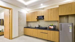 A modern kitchen with wooden cabinets, a stainless steel refrigerator, and a microwave. - Urban Alcove Executive Suites by Luxe 8 (Gurugram)
