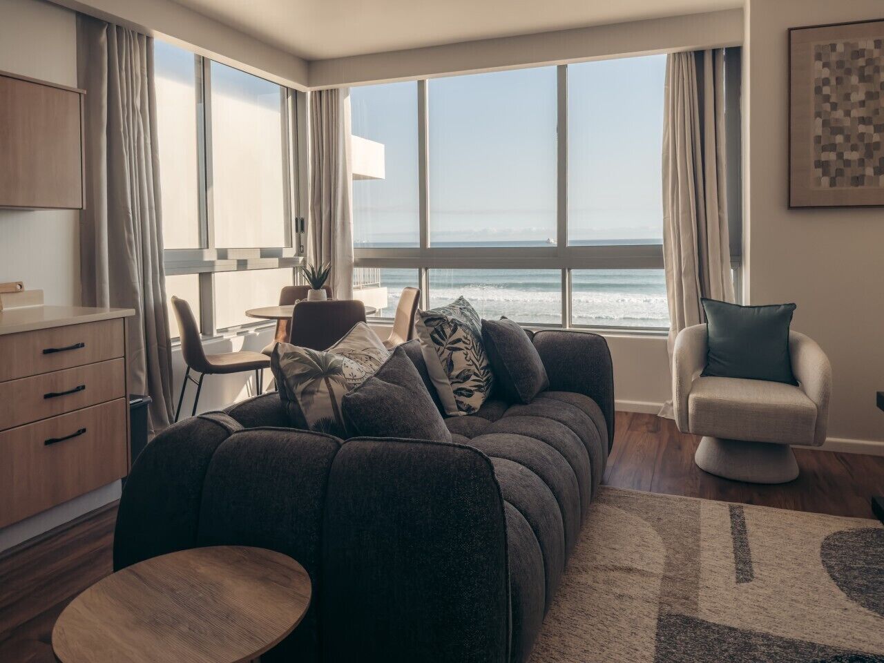 A modern living room with a sofa, a dining table, and a view of the sea.