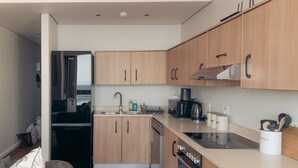 A compact kitchen with wooden cabinets, a built-in oven, and a coffee maker. - Infinity 2BR Seaside Stay - Steps from Blouberg Beach (Cape Town)