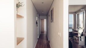 A hallway with wooden flooring leading to a dining area with a view of the ocean. - Infinity 2BR Seaside Stay - Steps from Blouberg Beach (Cape Town)
