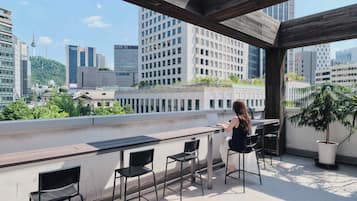 A rooftop terrace with a view of a cityscape, including a tower and various buildings.