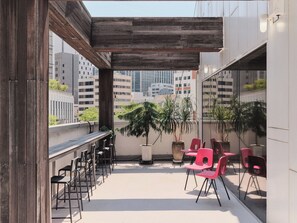 An outdoor terrace with a wooden pergola, seating area with chairs, and potted plants.