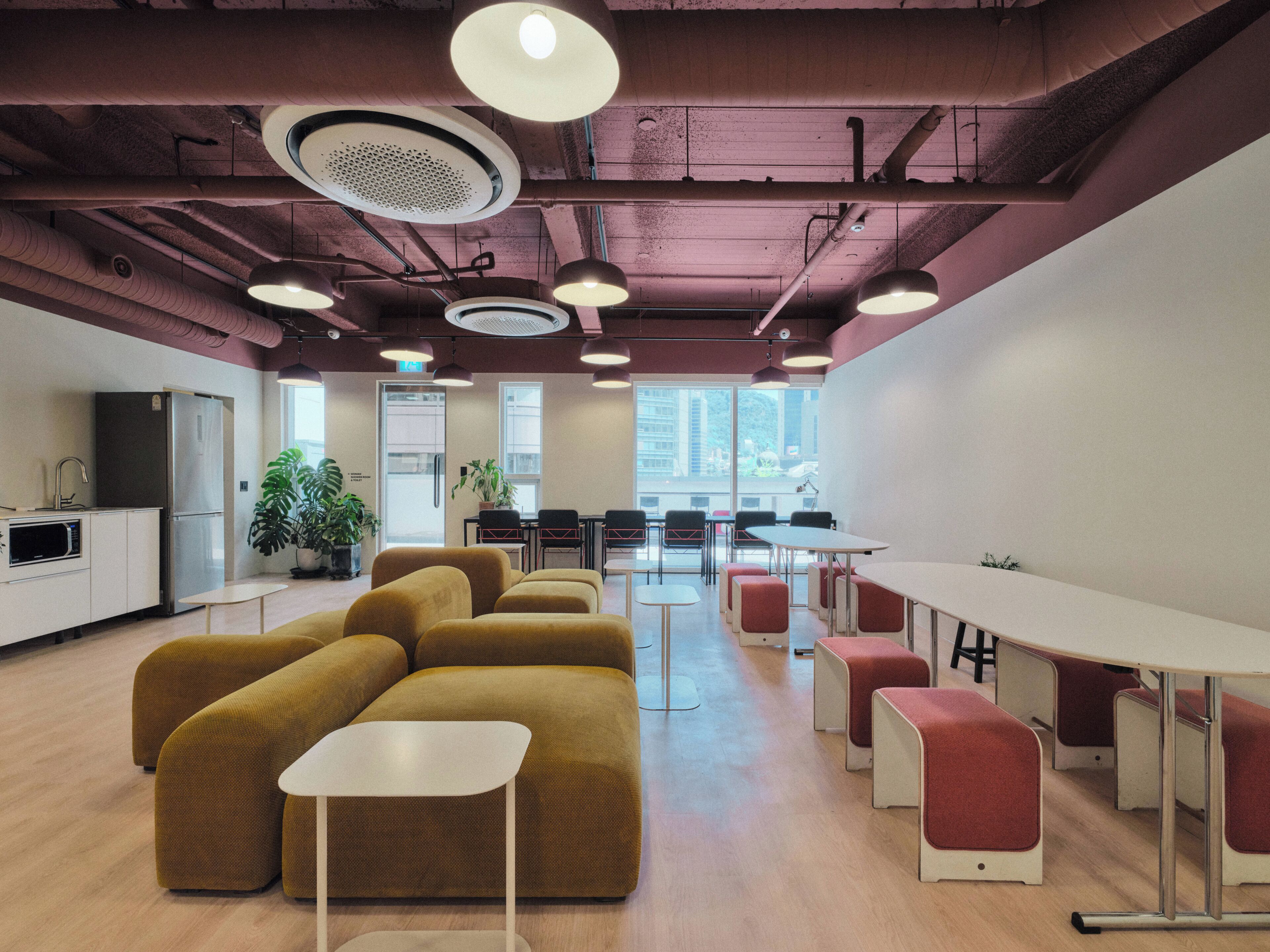 A modern office space with a kitchen area, seating arrangements, and large windows.