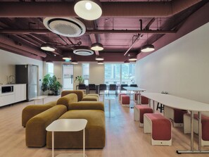 A modern office space with a kitchen area, seating arrangements, and large windows.