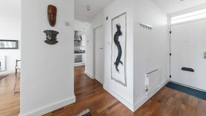 A hallway with wooden flooring, white walls, and artwork including a wooden mask and a black silhouette. - Airy 1BD Flat with Balcony, Battersea (Greater London)