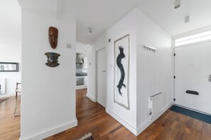 A hallway with wooden flooring, white walls, and artwork including a wooden mask and a black silhouette. - Airy 1BD Flat with Balcony, Battersea (Greater London)