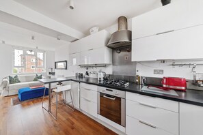 A modern kitchen with white cabinets, a stainless steel range hood, and a red toaster. - Airy 1BD Flat with Balcony, Battersea (Greater London)