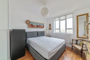 A bedroom with a bed, a wardrobe, a chair, a window with a view, and a wall-mounted mirror. - Airy 1BD Flat with Balcony, Battersea (Greater London)