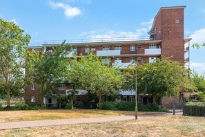 A multi-story residential building with a brick facade, balconies, and a paved walkway in front. - Airy 1BD Flat with Balcony, Battersea (Greater London)