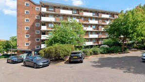 A multi-story residential building with a brick facade, multiple balconies, and a parking area with cars. - Airy 1BD Flat with Balcony, Battersea (Greater London)