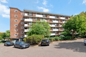 A multi-story residential building with a brick facade, multiple balconies, and a parking area with cars. - Airy 1BD Flat with Balcony, Battersea (Greater London)