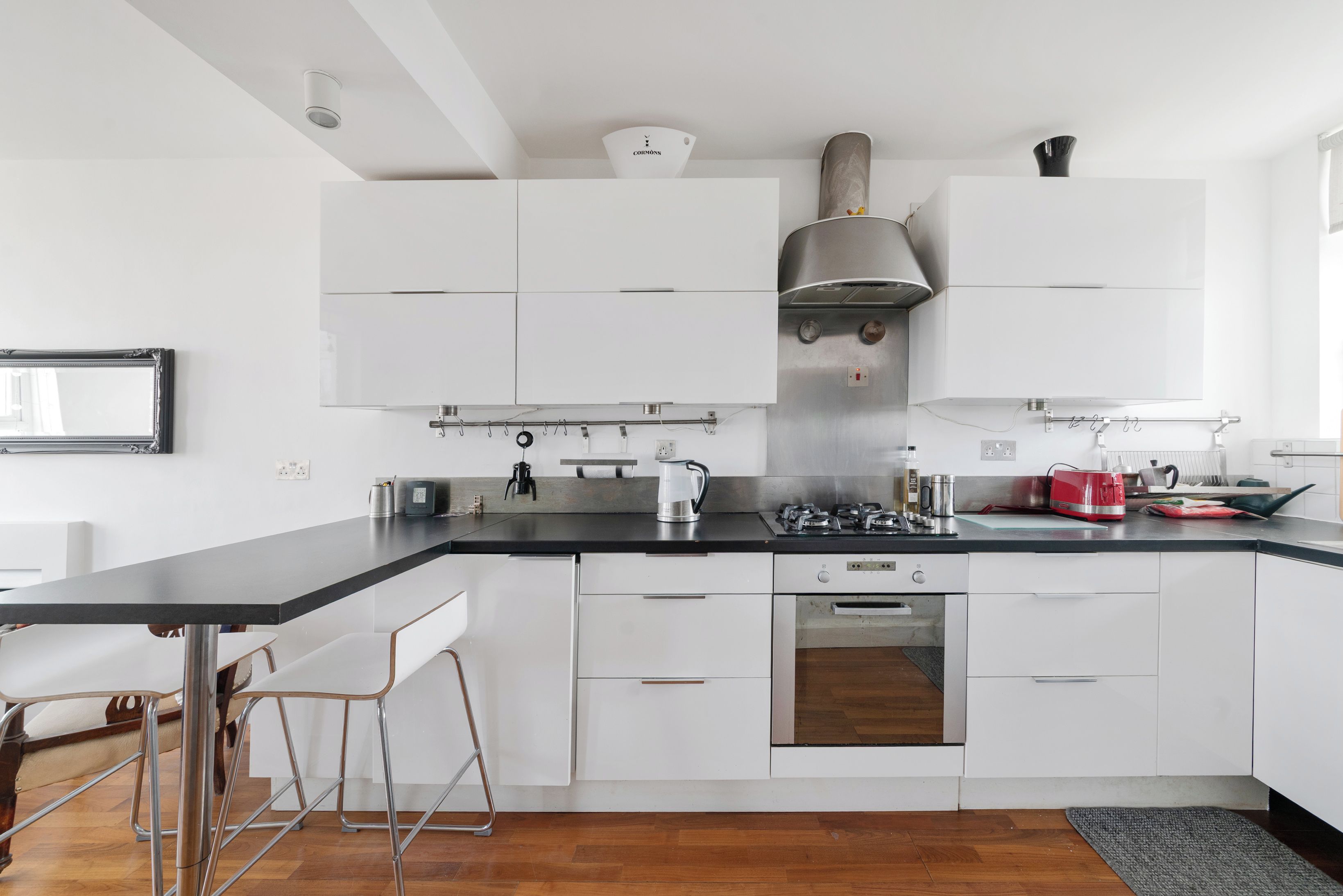 Een moderne keuken met witte kasten, een zwart aanrecht, roestvrijstalen apparatuur en een barkruk.