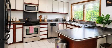 A modern kitchen with a central island, stainless steel appliances, and a window with blinds.