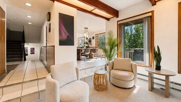 Amplia sala de estar con sofá, sillón y una mesita, una escalera que sube a otro nivel, y un ventanal con vistas a la vegetación.