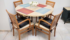 A round wooden table with a colorful tablecloth, surrounded by four wooden chairs with black cushions. - Pantheon - A Cozy Nest in the Center of Athens (Athina)