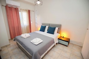 A hotel room with a bed, a nightstand, a lamp, and a window with curtains. - Pantheon - A Cozy Nest in the Center of Athens (Athina)
