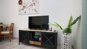 A living room with a TV on a black cabinet, a painting on the wall, and a potted plant. - Pantheon - A Cozy Nest in the Center of Athens (Athina)
