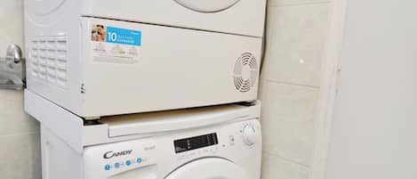 A stacked washer and dryer unit in a corner of a room with tiled flooring.