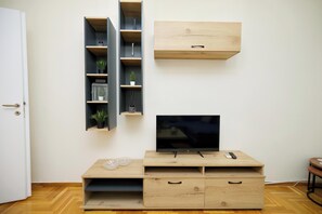 Una sala de estar con televisor sobre un mueble de madera, una mesita y estanterías empotradas con plantas.