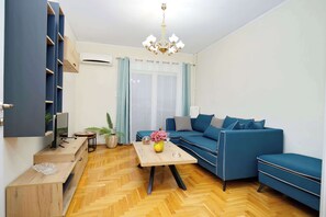 Ein modernes Wohnzimmer mit einem blauen Sofagarnitur, einem Holztisch und einem Fernseher auf einem Holzgestell.