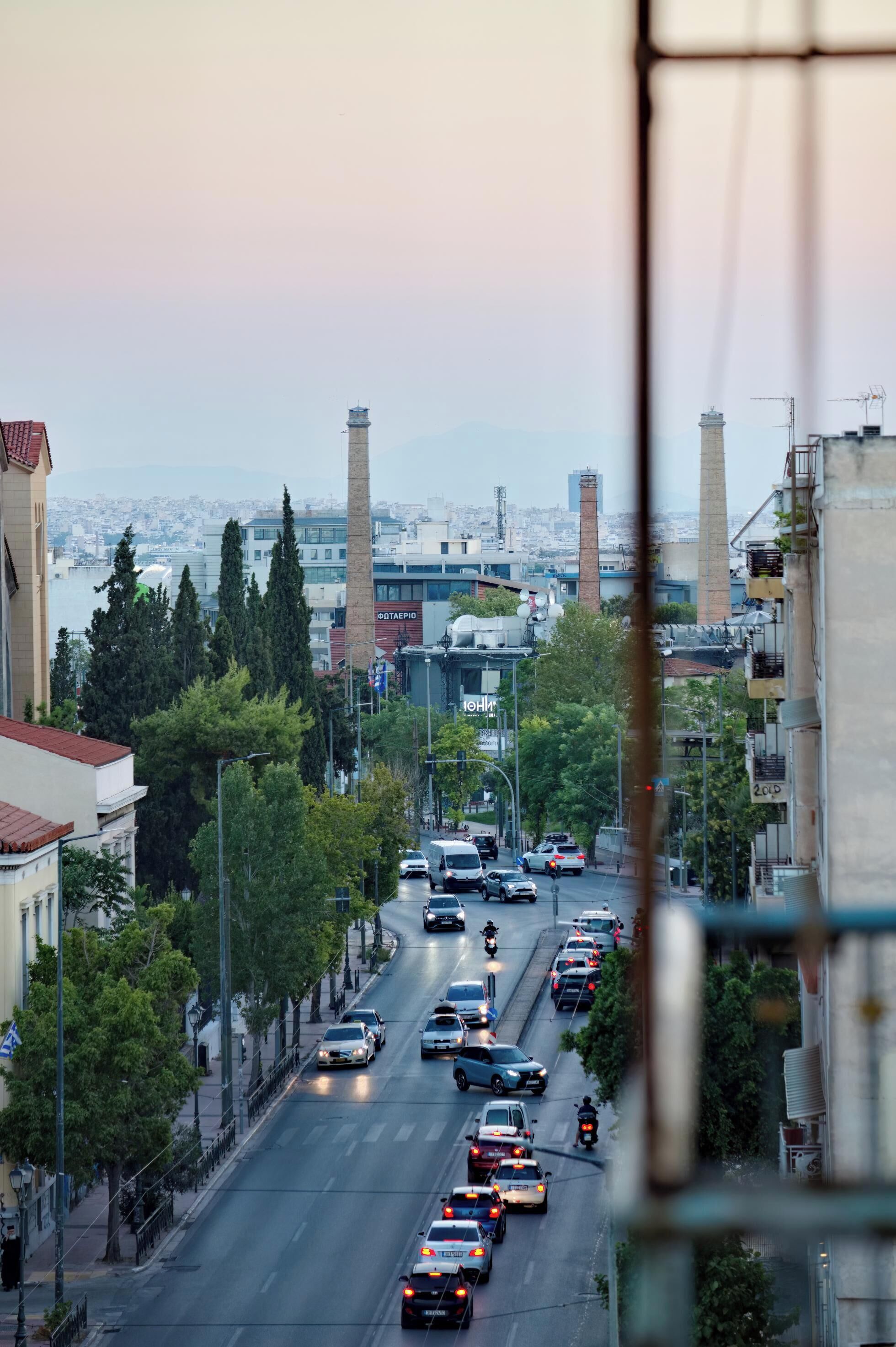 Une rue animée en milieu urbain, avec plusieurs voies de circulation, des immeubles et des arbres.