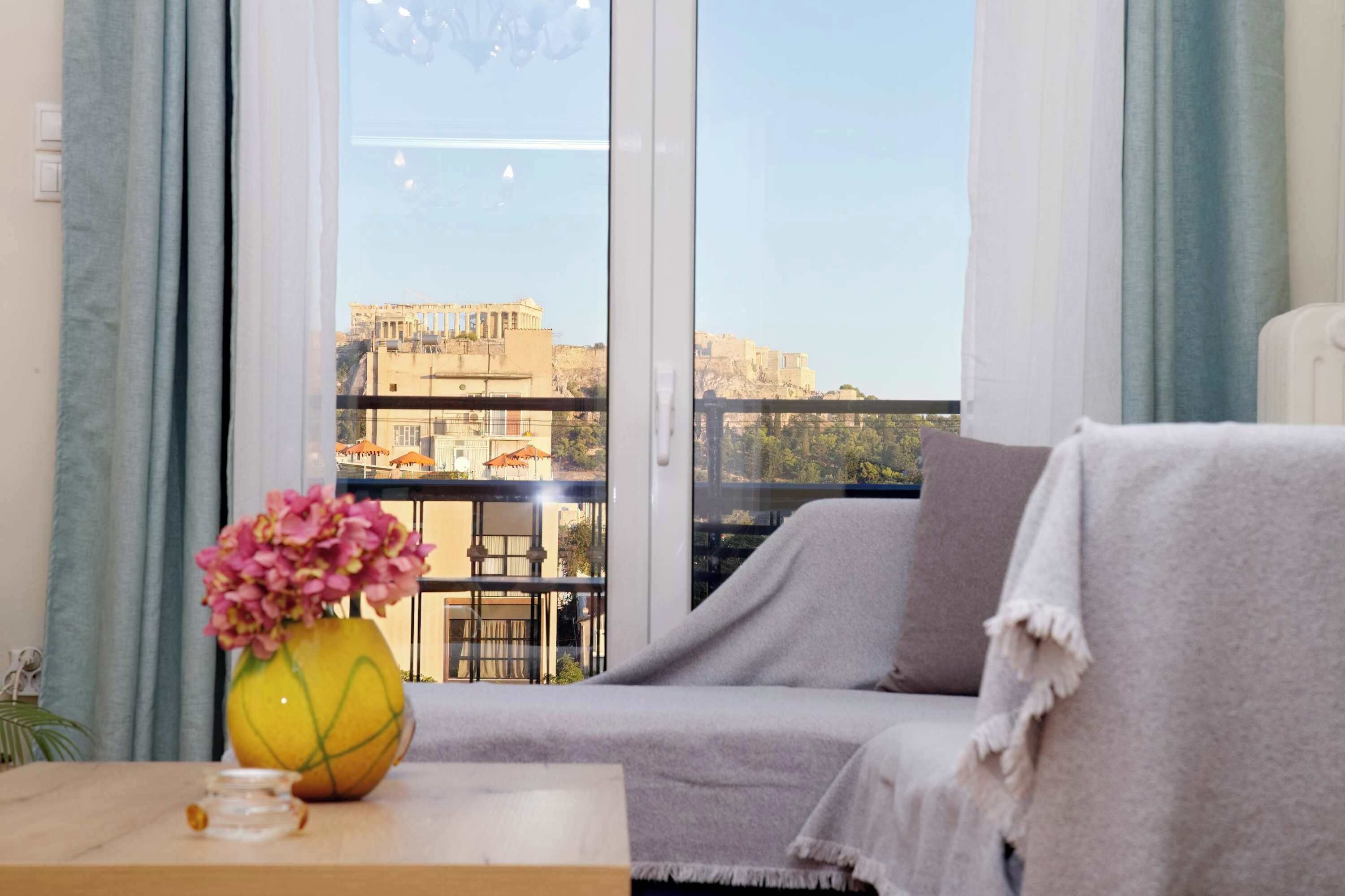 A balcony with a sofa, a vase with flowers, and a view of ancient ruins.