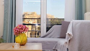 Ein Balkon mit einer Couch, einer Blumenvase und Blick auf alte Ruinen.