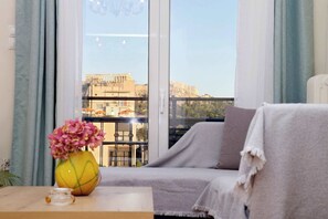 Ein Balkon mit einer Couch, einer Blumenvase und Blick auf alte Ruinen.