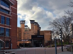 Ein Gebäude mit einem markanten Bibliothekeneingang, umgeben von moderner Architektur und blauem Himmel.