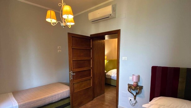 A room with two beds, a wooden wardrobe, a hanging light fixture, an air conditioning unit, and a bedside table with a lamp. - La Rocca Guest House & SPA - Family Superior Room 2 (Montefalco)