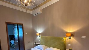 A hotel room with a large bed, a chandelier, wall-mounted lamps, and a door leading to another room. - La Rocca Guest House & SPA - Family Superior Room 2 (Montefalco)