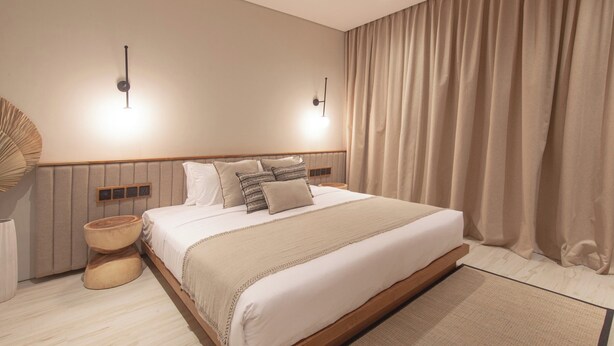 A modern bedroom with a wooden bed frame, a bedside table, a wall-mounted lamp, and a large window with curtains. - East 88 Unit 3 (Badung)