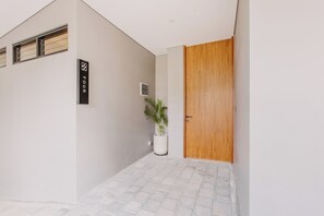 A modern entrance with a wooden door, a potted plant, and a sign indicating the room number. - East 88 Unit 3 (Badung)
