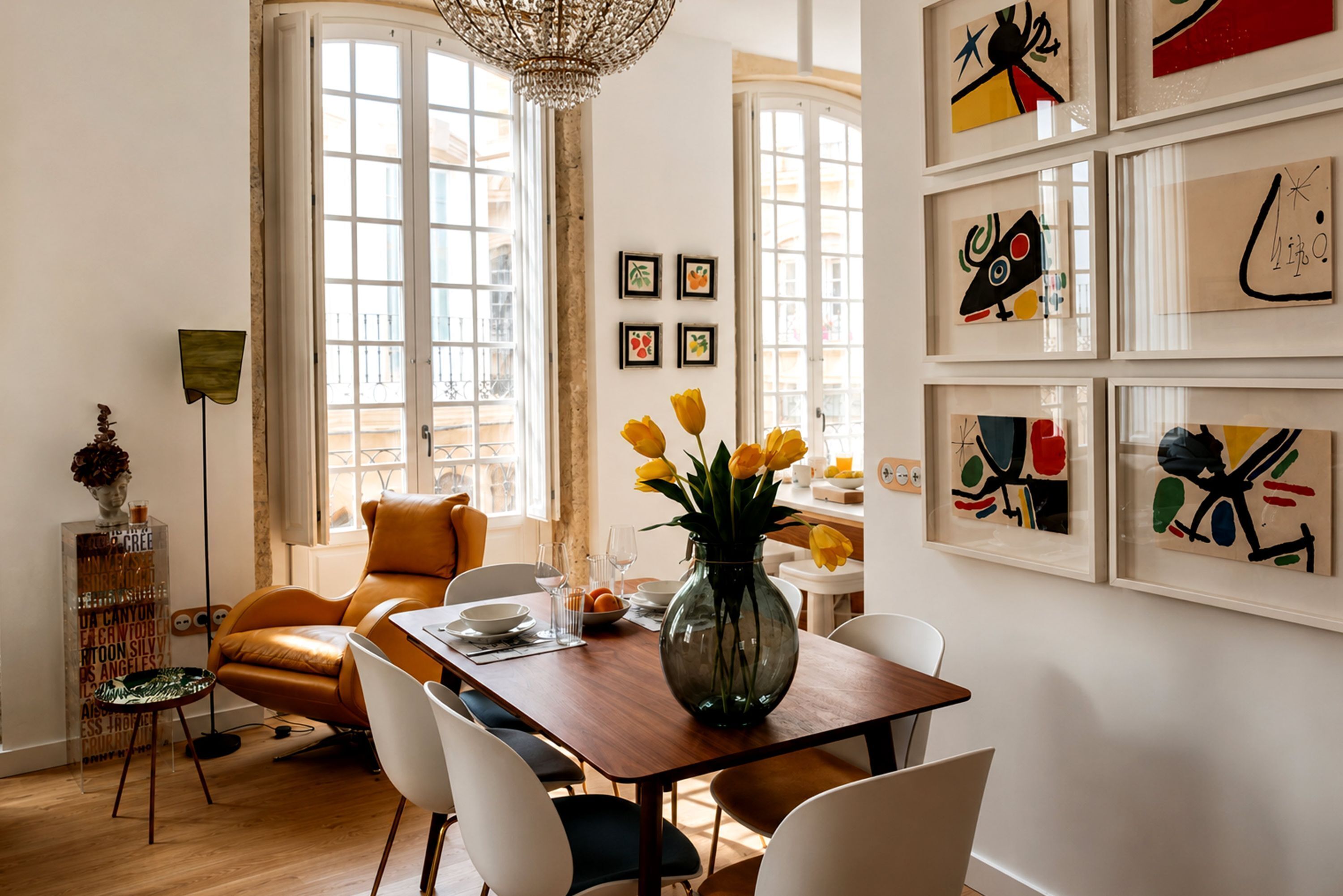 A dining area with a wooden table, white chairs, and a vase with yellow flowers.