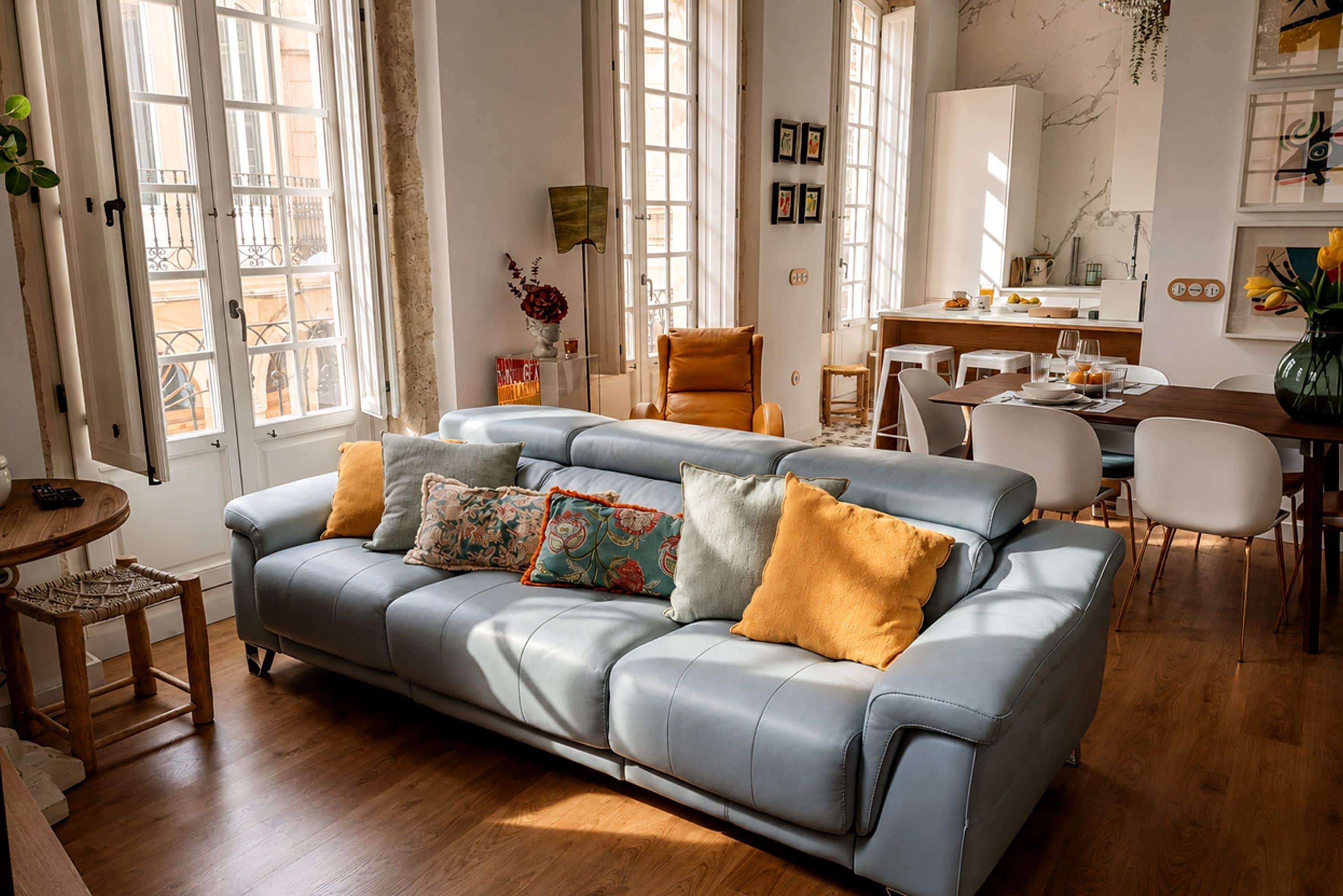 A modern living room with a grey sofa, wooden flooring, and a dining area with a white table and chairs.