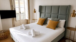 A neatly made bed with white linens and two pillows, a television mounted on the wall, and a window with curtains. - Genteel Home Casa Leal de Ibarra (Almeria)
