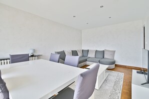 A modern living room with a white sofa, a dining table, and a flat-screen TV. - Apartment '3 chambres Vue Montagnes -' (Annecy)