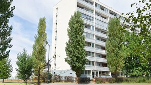 Ein mehrstöckiges Gebäude mit flacher Fassade, umgeben von Bäumen und blauem Himmel.