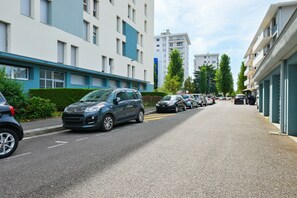 A residential street with parked cars, modern apartment buildings, and a clear sky. - Spacious T4 Apartment with Mountain Views, Wi-Fi, and Parking – Sleeps 8 in Annecy (Annecy)