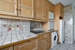 A kitchen with wooden cabinets, a microwave, a stove, a washing machine, and tiled backsplash with floral patterns. - Apartment '3 chambres Vue Montagnes -' (Annecy)
